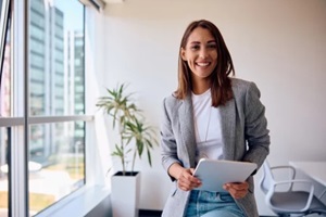 happy businesswoman using touchpad while working in office and looking at camera