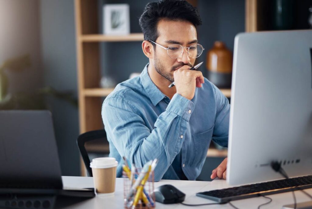 Serious, business man and thinking on computer in office, internet research and website. Focused male employee, desktop and solution of ideas, planning decision and review strategy, project or vision.